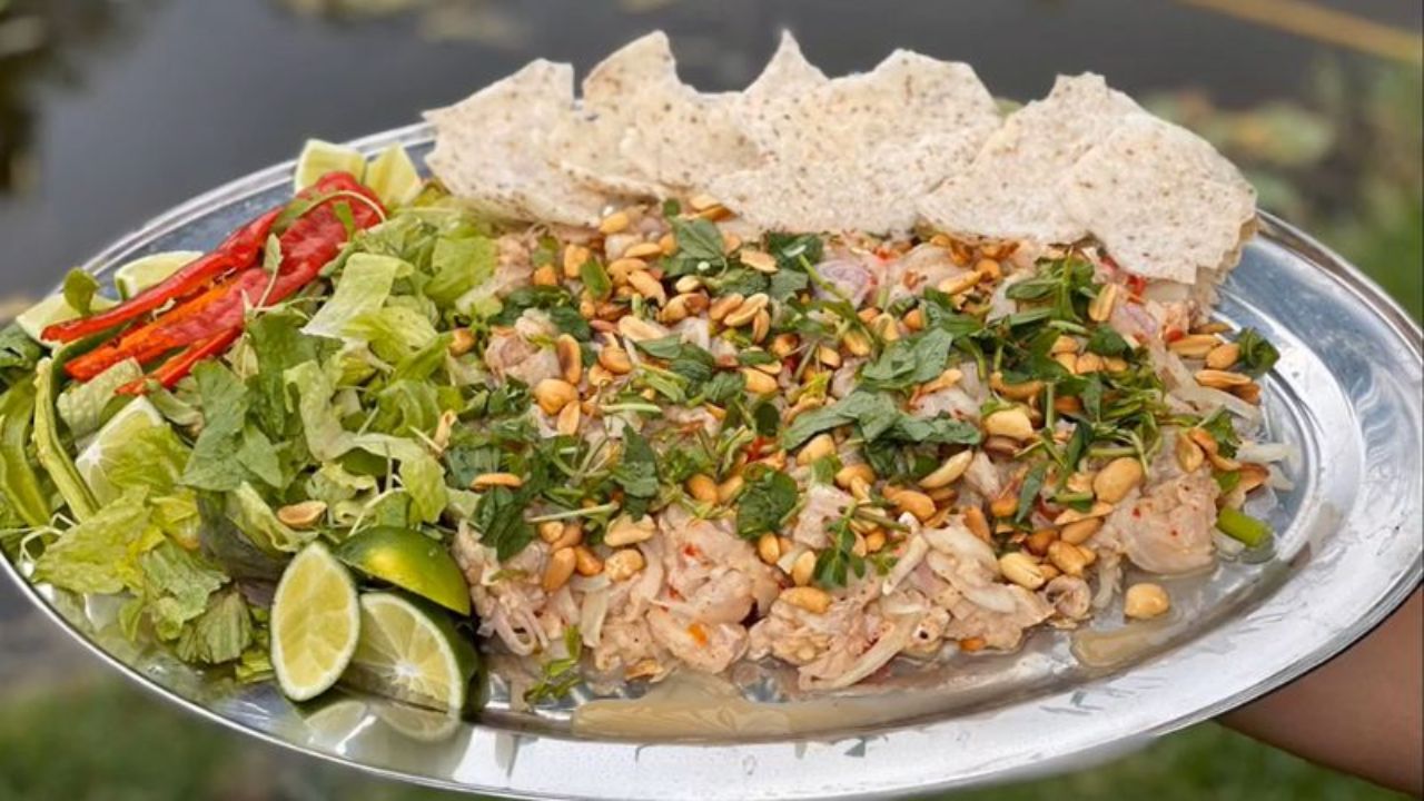 Chén gỏi cá nhám trộn đều cùng các loại rau thơm, khế chua và đậu phộng rang, dọn kèm bánh tráng nướng giòn rụm
